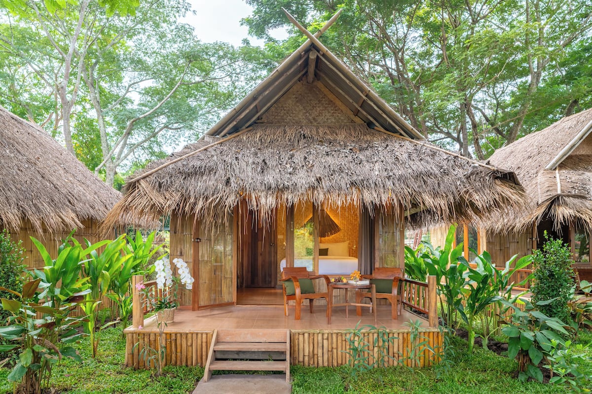 A thatched-roof hut with a wooden deck, surrounded by lush greenery.