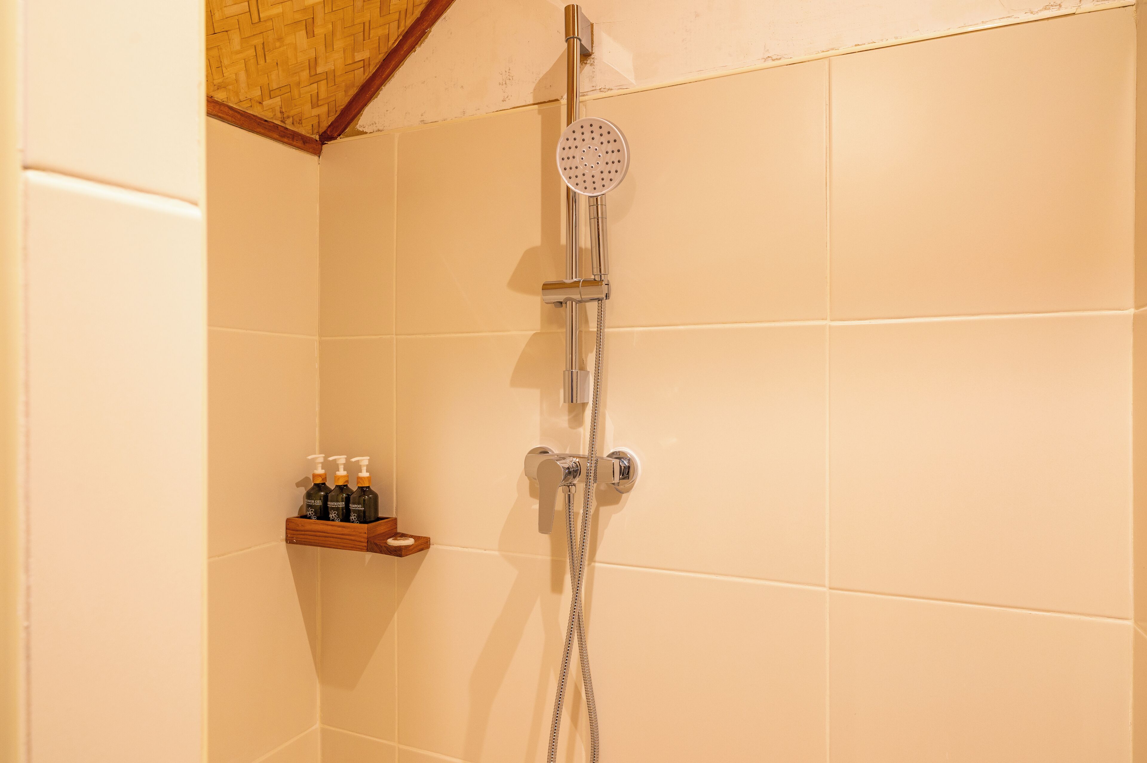 A shower with a handheld showerhead and a wall-mounted faucet. There is a wooden shelf with toiletries.