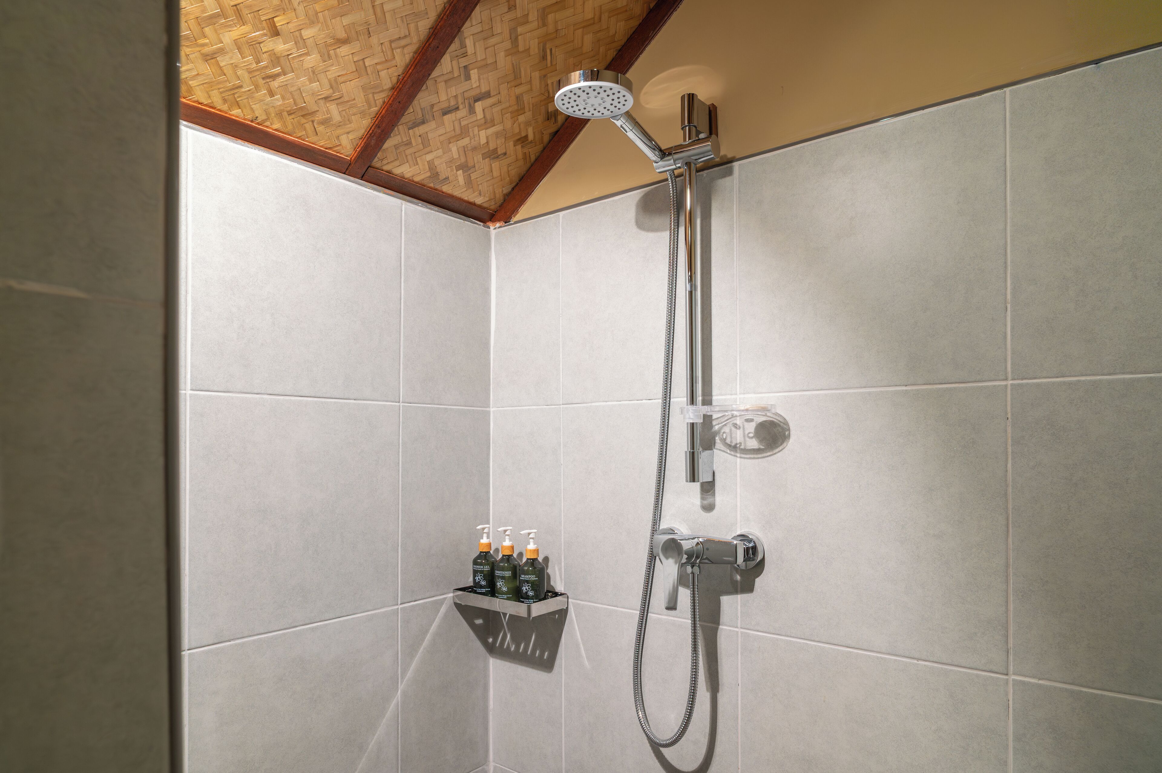 Zona de ducha con cabezal de ducha de mano, grifería empotrada en la pared y estante con artículos de aseo.
