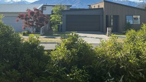 Et moderne hus med garage, omgivet af frodigt grønt og med et bjerg i baggrunden.