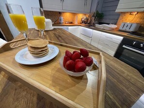 Ein Frühstücksbrett mit Pfannkuchen, Erdbeeren und Orangensaftgläsern auf einem Holztisch in einer Küche.