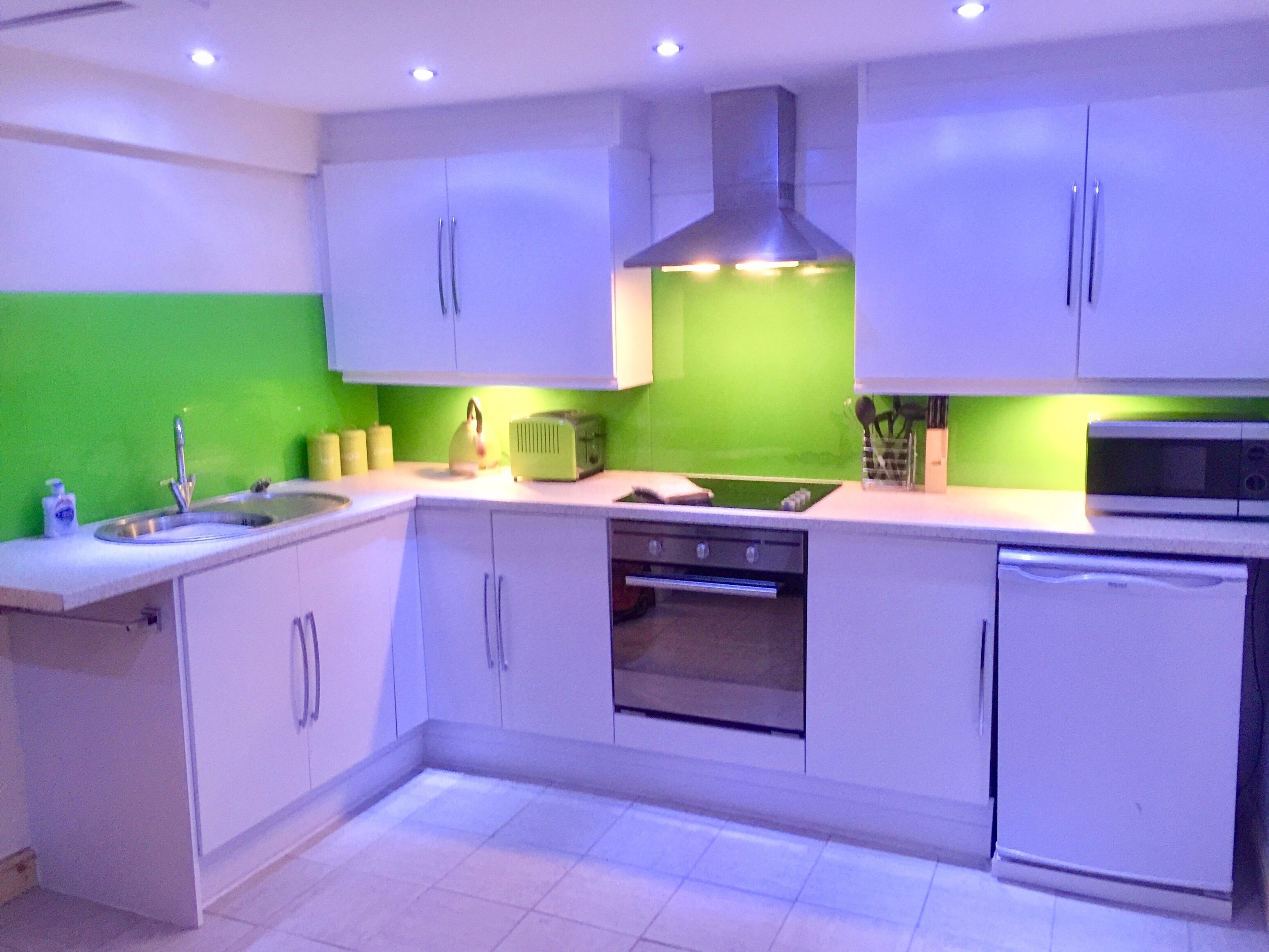A modern kitchen with white cabinets, a green backsplash, a built-in oven, and a microwave.