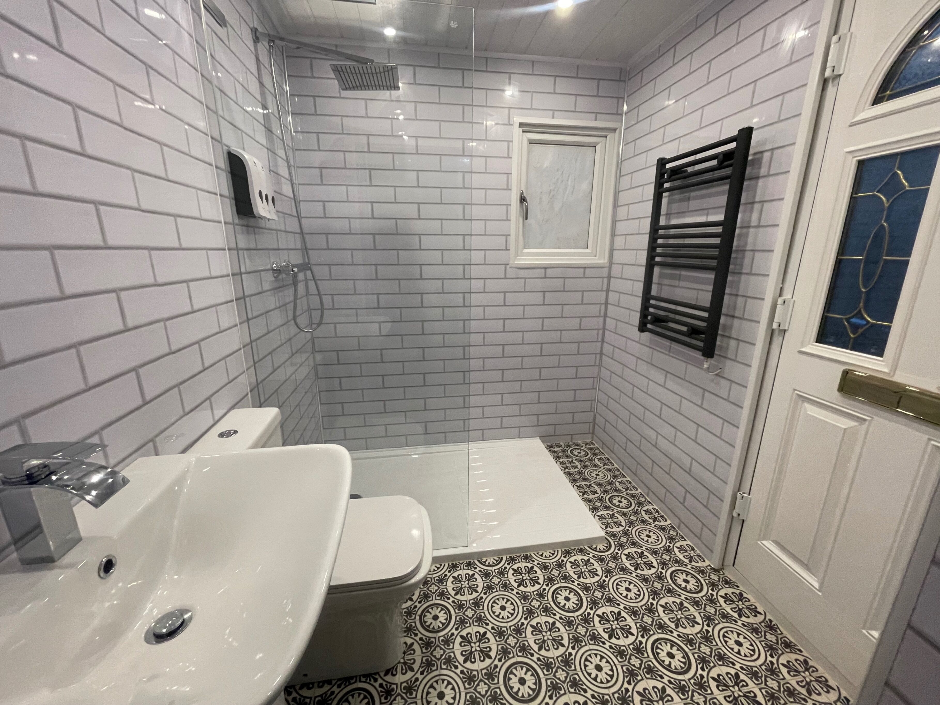 A bathroom with white subway tiles, a black and white patterned floor, a white door, and a towel rack.