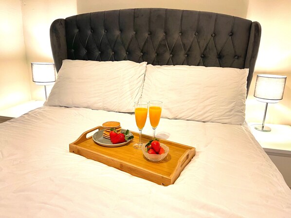 A neatly made bed with a wooden tray holding breakfast items, including pancakes, strawberries, and orange juice glasses.