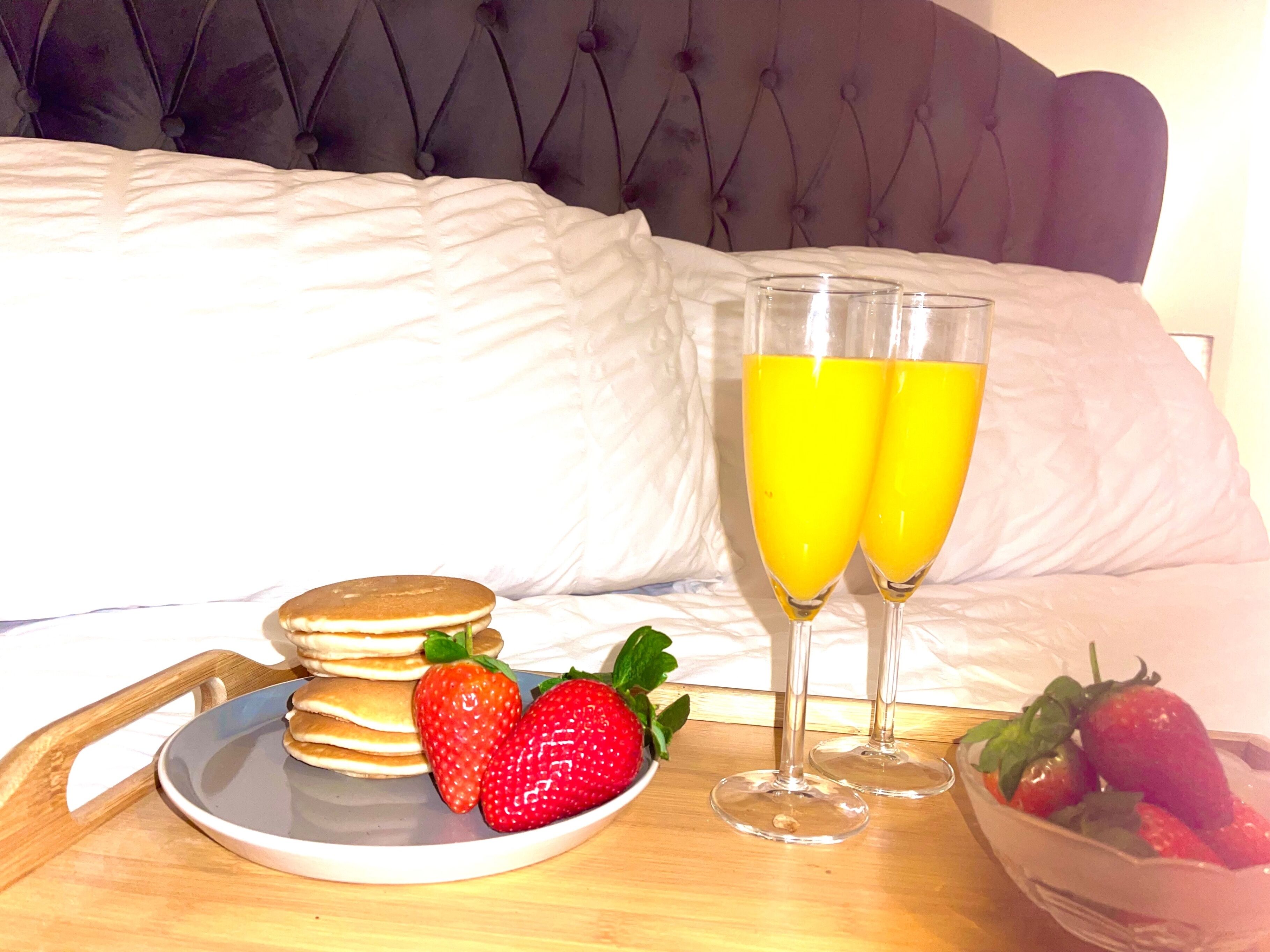 Colazione con pancake, fragole e succo d'arancia su un vassoio.