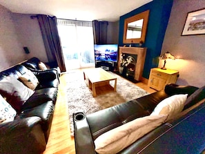 A living room with a black leather sofa, a wooden coffee table, a fireplace, and a television.