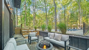 An outdoor patio with a fire pit, seating, and a view of a forest. - The Whispering Hollow – Private Pool, Hot Tub & Forest Escape Near Beach (Union Pier)
