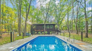 A swimming pool with a wooden deck and a house in the background surrounded by trees. - The Whispering Hollow – Private Pool, Hot Tub & Forest Escape Near Beach (Union Pier)