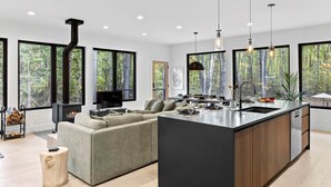 A modern kitchen with a large island, built-in appliances, and large windows offering a forest view. - The Whispering Hollow – Private Pool, Hot Tub & Forest Escape Near Beach (Union Pier)