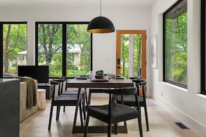 A dining area with a table set for four, surrounded by chairs, a pendant light, and a view of a forest through large windows. - The Whispering Hollow – Private Pool, Hot Tub & Forest Escape Near Beach (Union Pier)