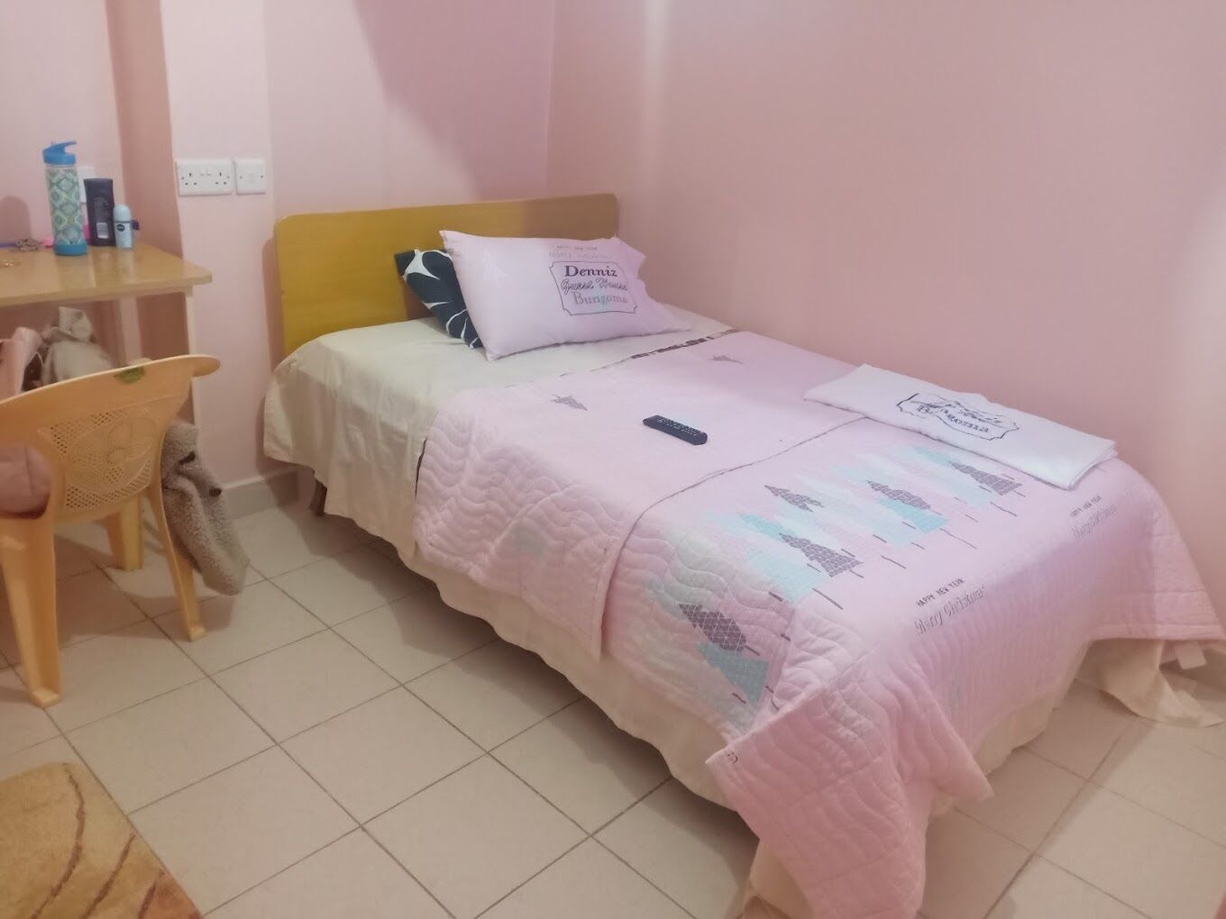 A small, neatly arranged bedroom with a single bed, a chair, and a desk with personal items.