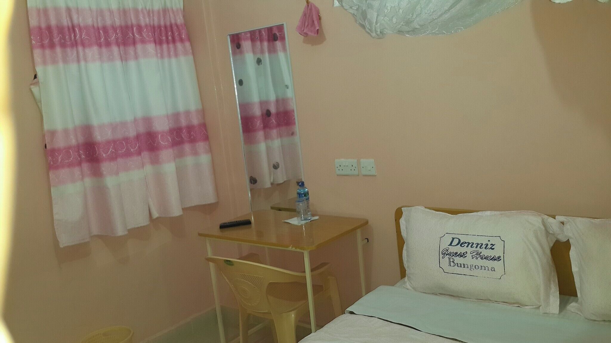 A bedroom with a bed, a desk, a chair, a mirror, and a wall-mounted curtain.