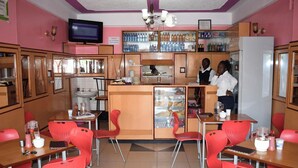A cafeteria with red chairs, wooden tables, a refrigerator, and a counter with beverages. - Denniz Guest House Bungoma (Bungoma)