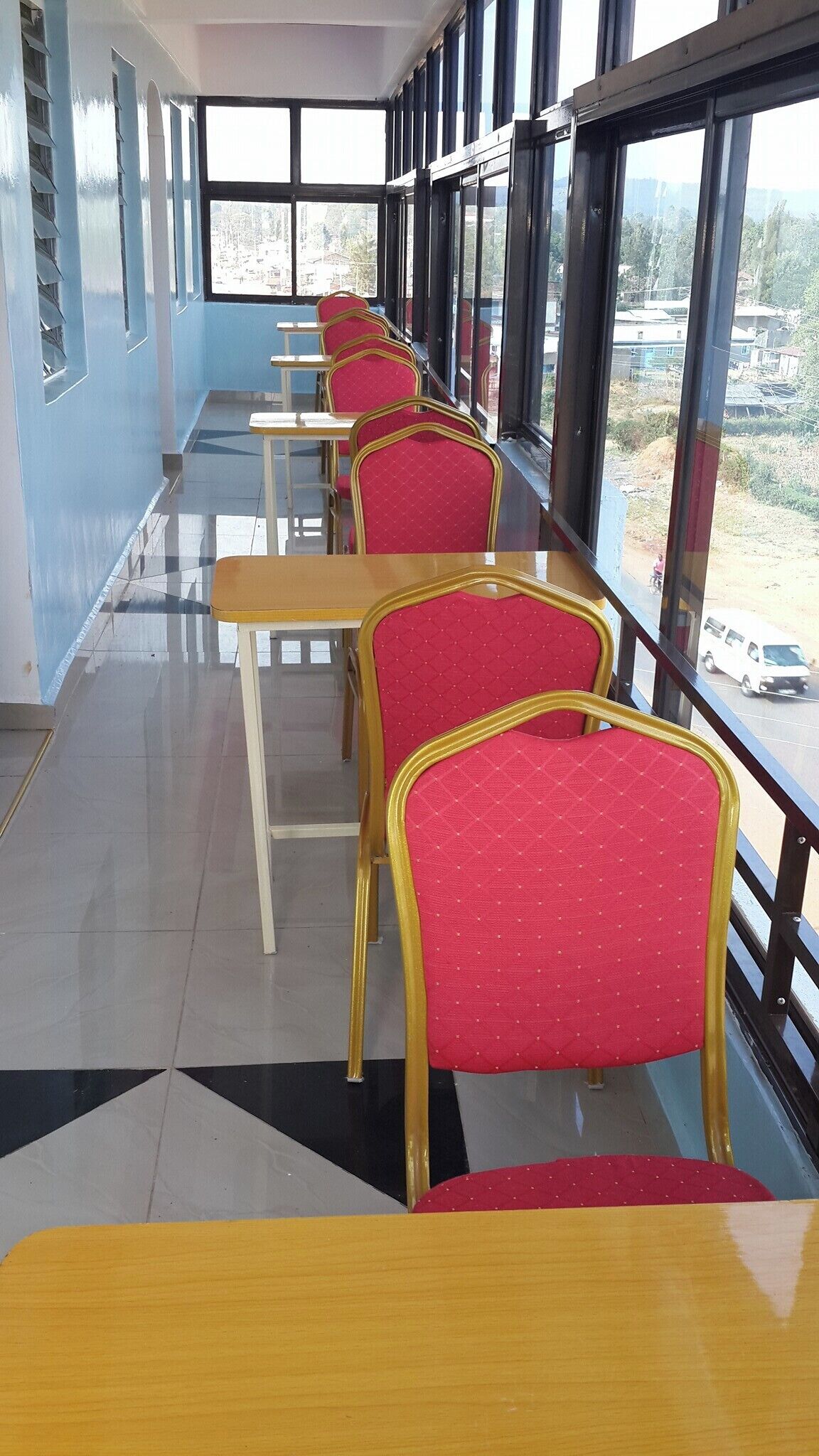 A row of red chairs with gold frames and wooden tables in a room with large windows.