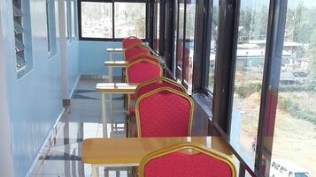 A row of red chairs with gold frames and wooden tables in a room with large windows.