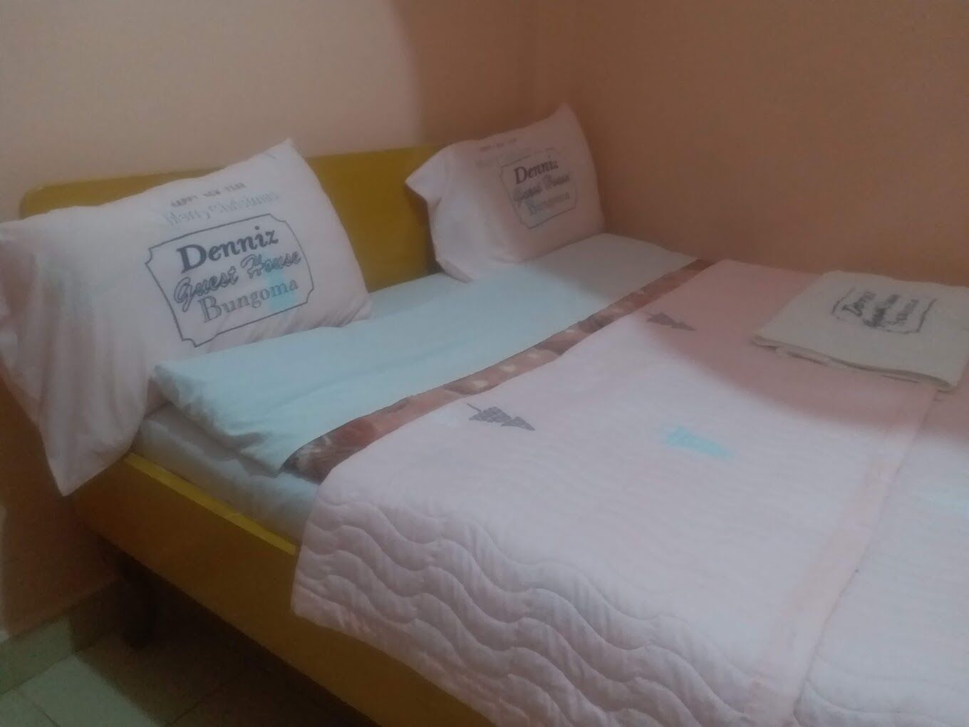 Uma cama de solteiro com cabeceira amarela, almofadas e cobreleira brancas.