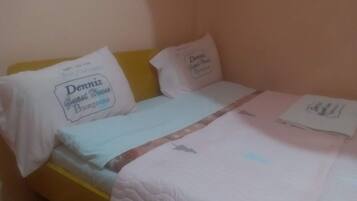 Uma cama de solteiro com cabeceira amarela, almofadas e cobreleira brancas.