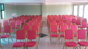 A conference room with rows of pink chairs and gold frames, arranged in a U-shape with a black podium at the front. - Denniz Guest House Bungoma (Bungoma)