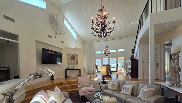 A spacious living room with a large chandelier, a television, and a staircase leading to an upper level. - Haven Getaway Inground Pool Inground Hot tub Family (Belton)