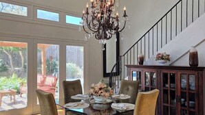 A dining area with a chandelier, wooden dining table, cushioned chairs, and a view of the outdoors. - Haven Getaway Inground Pool Inground Hot tub Family (Belton)