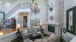 A spacious living area with a staircase, a chandelier, a fireplace, and a mounted deer head. - Haven Getaway Inground Pool Inground Hot tub Family (Belton)
