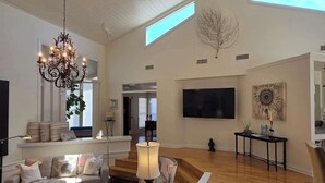 A spacious living room with a high ceiling, a chandelier, a flat-screen TV, and a large window. - Haven Getaway Inground Pool Inground Hot tub Family (Belton)