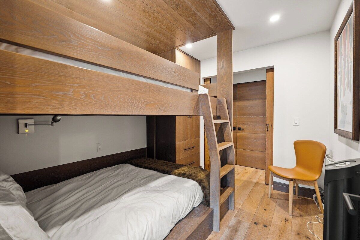 Un lit superposé avec une échelle, un bureau, une chaise et une armoire, dans une pièce au plancher en bois et aux murs blancs.