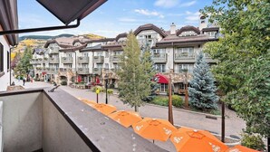 Een hotel met meerlaags gebouwen, buiten zitplaatsen met oranje parasols, en uitzicht op een bergachtig landschap.