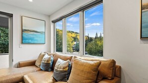 Een kamer met een groot raam, een bank met kussens en een schilderij aan de muur.