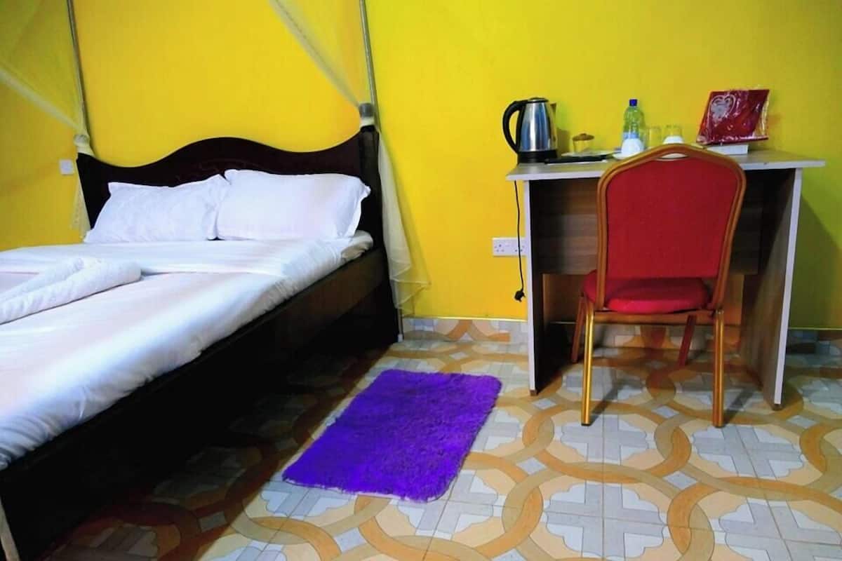 A room with a bed, a desk with a chair, a purple rug, and a yellow wall.