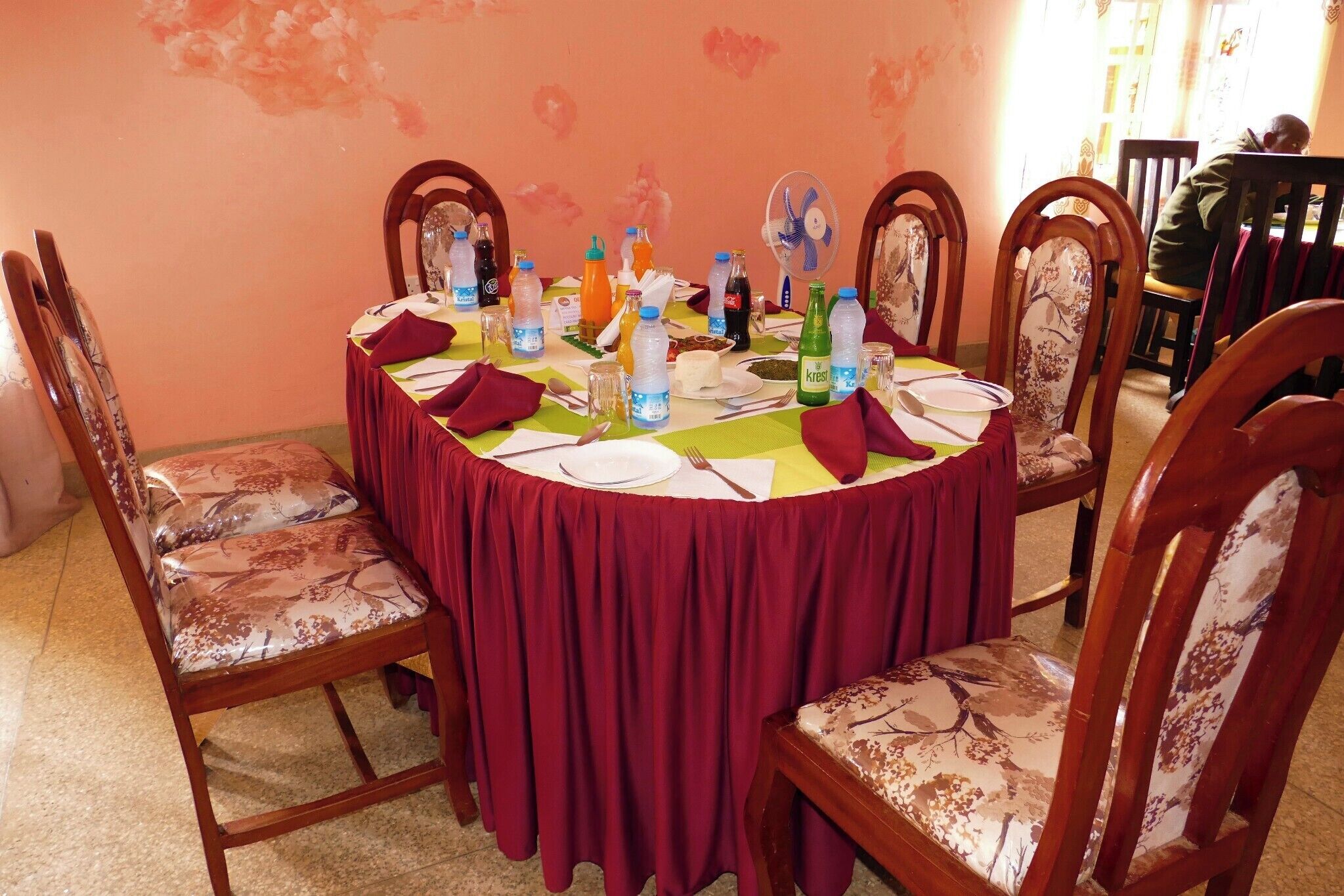 A round dining table with a red tablecloth, surrounded by wooden chairs with floral upholstery.
