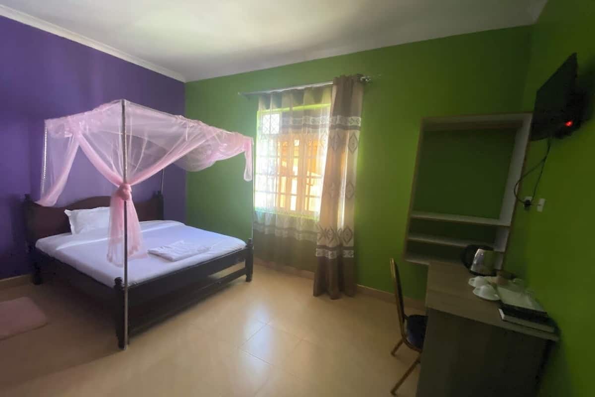 A bedroom with a bed, a desk, a chair, and a window with curtains.