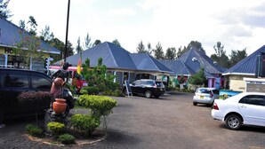 Un'area di parcheggio con diverse automobili, una statua e edifici con cartelli che indicano 'WASH ROOMS' e 'LADIES'.