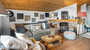 Een gezellige woonkamer met een houten plafond, een open haard, een bank en een salontafel.
