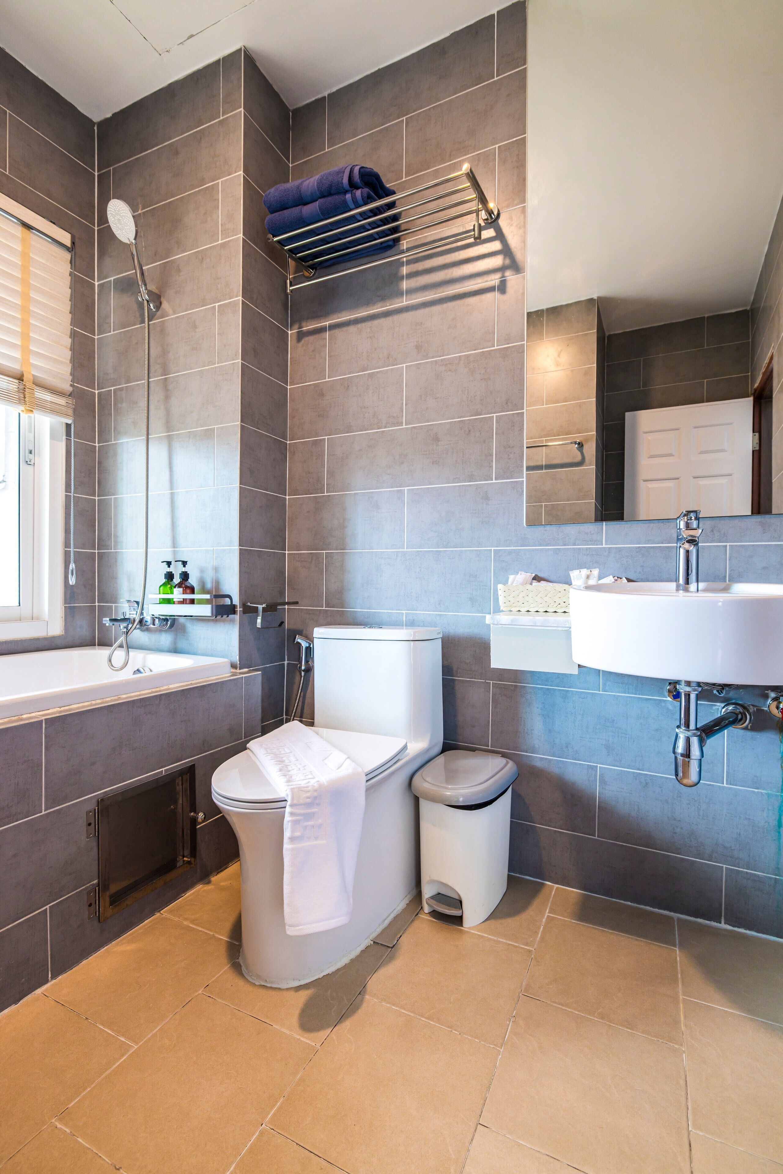Un baño moderno con bañera, inodoro y lavabo, con azulejos grises y un perchero para toallas.