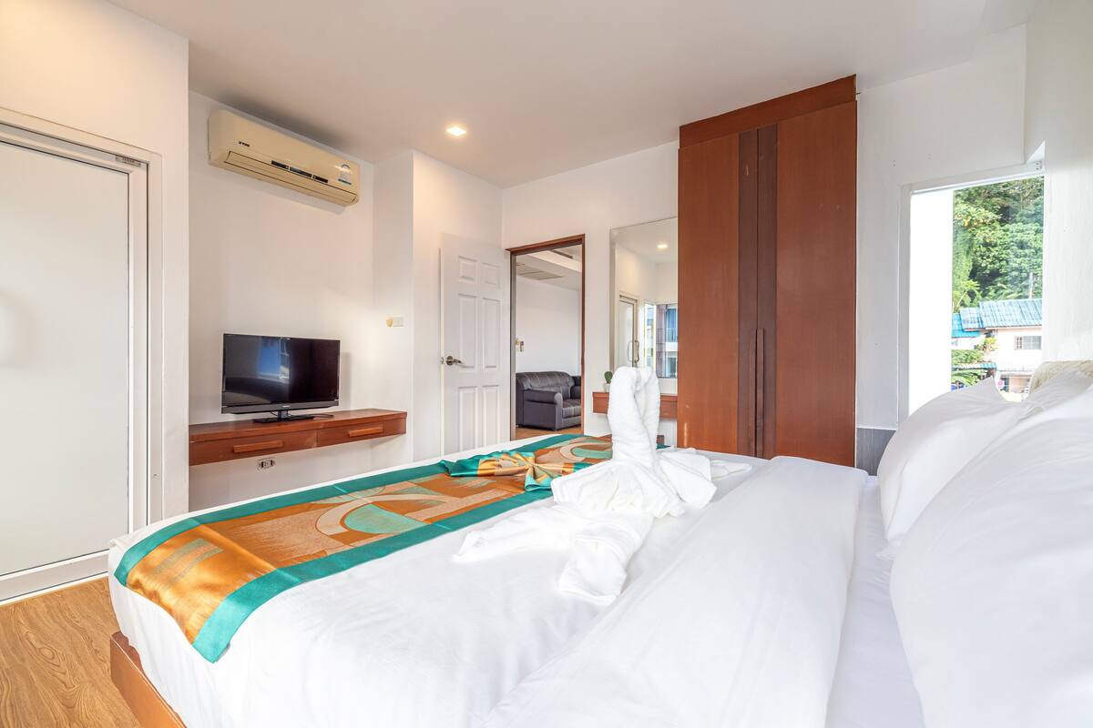A hotel room with a bed, a TV, an air conditioner, and a view of the outside.