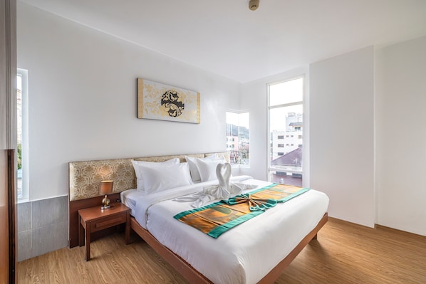 A hotel room with a large bed, a nightstand, a lamp, a window with a city view, and a wall-mounted artwork. - Aura Hotel Phuket (Patong)
