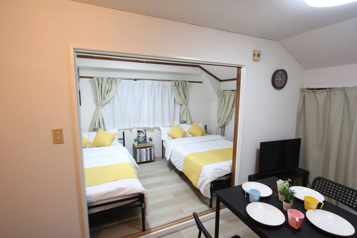 A hotel room with two beds, a TV, a table with plates, cups, and a small plant.