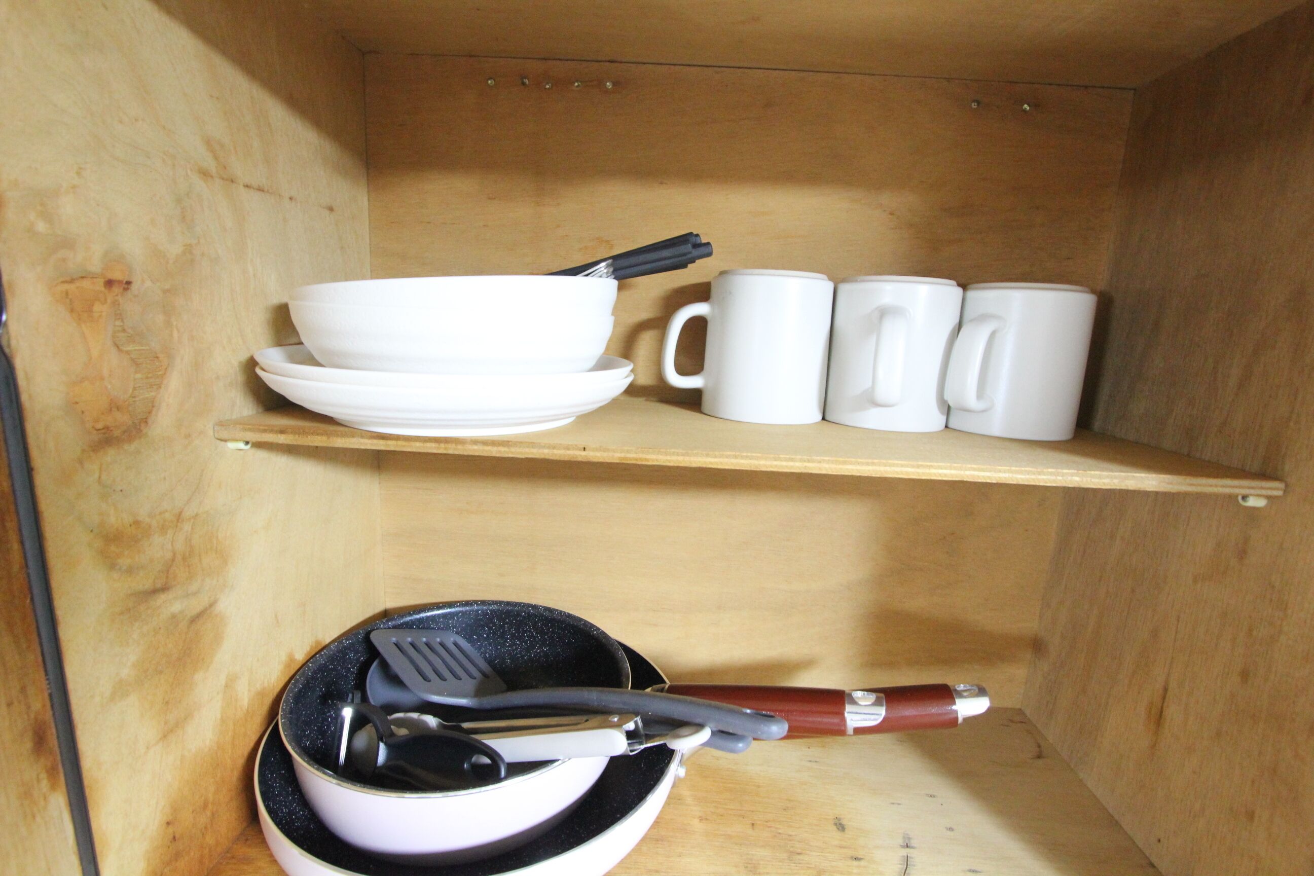 A kitchen with wooden shelves holding white bowls, plates, and mugs.