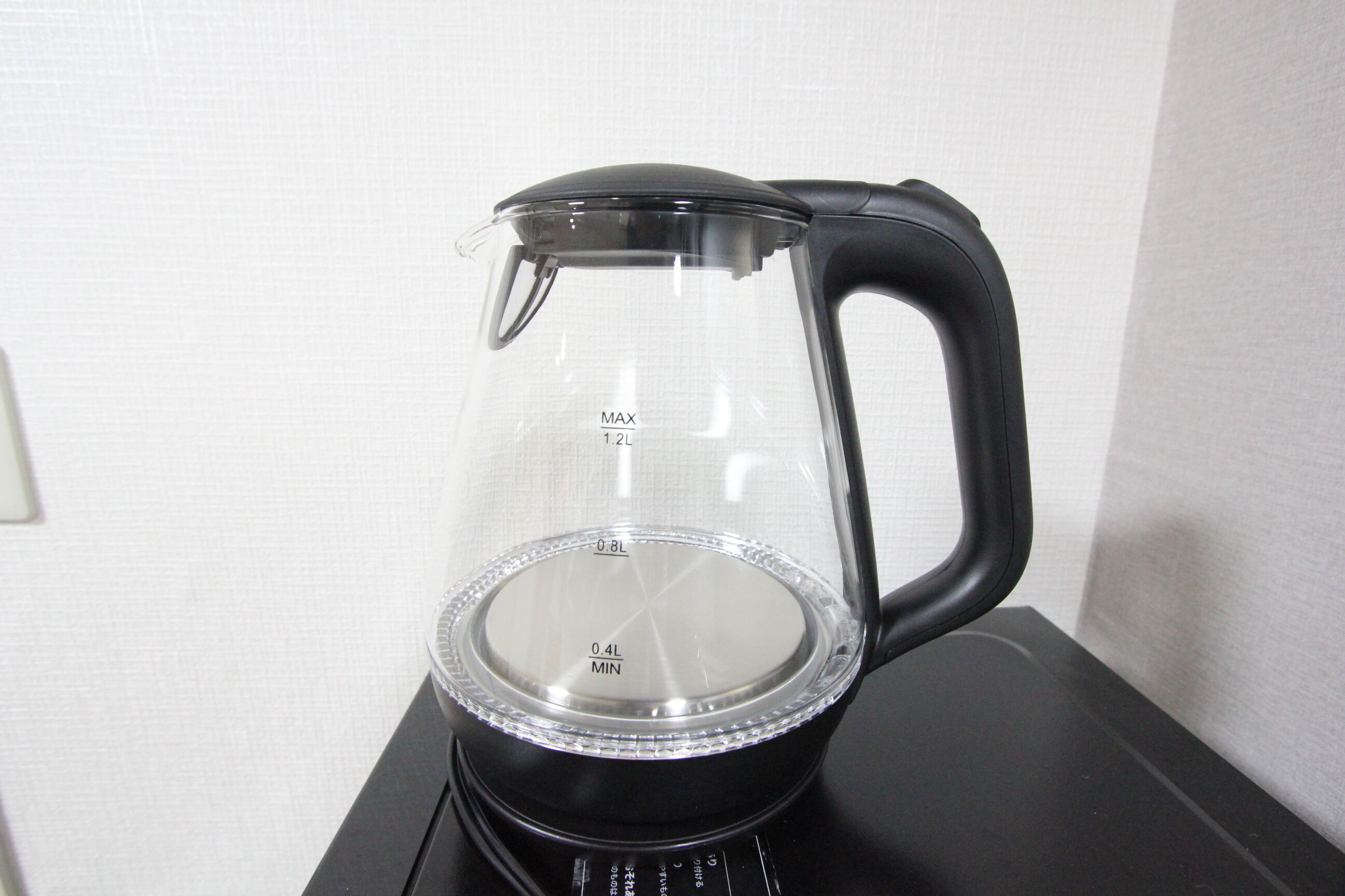 A clear glass water jug with measurement markings on a black base.