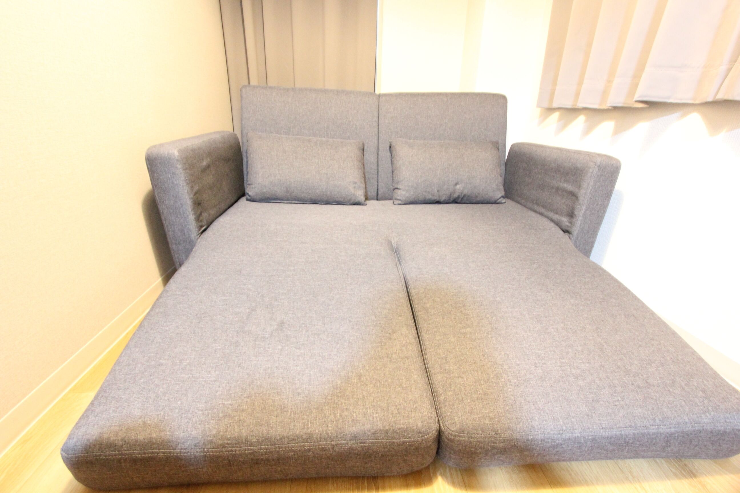 A grey sofa bed with a headboard and two pillows.