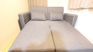 A grey sofa bed with a headboard and two pillows.