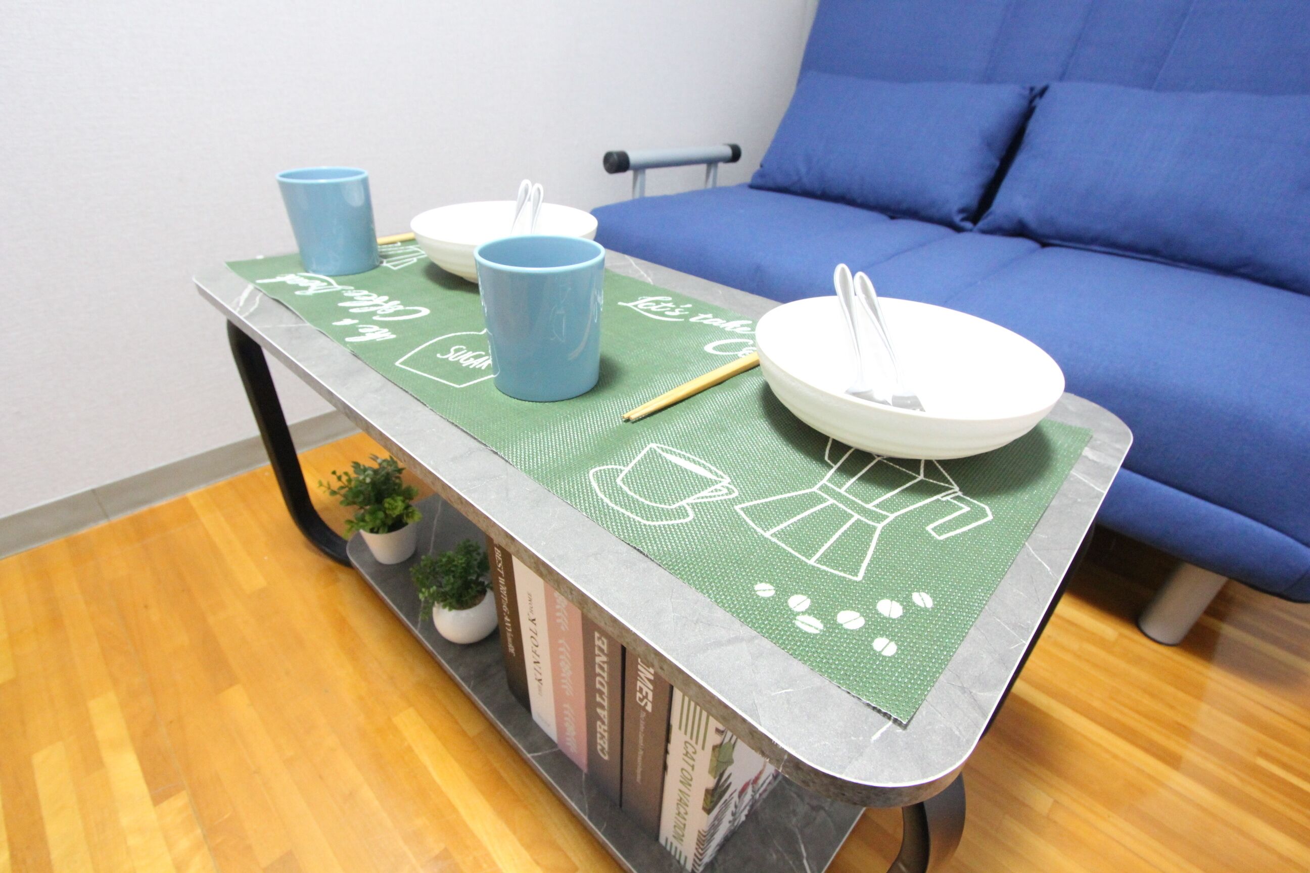 A small table with a green placemat, two blue cups, a white bowl, and chopsticks.