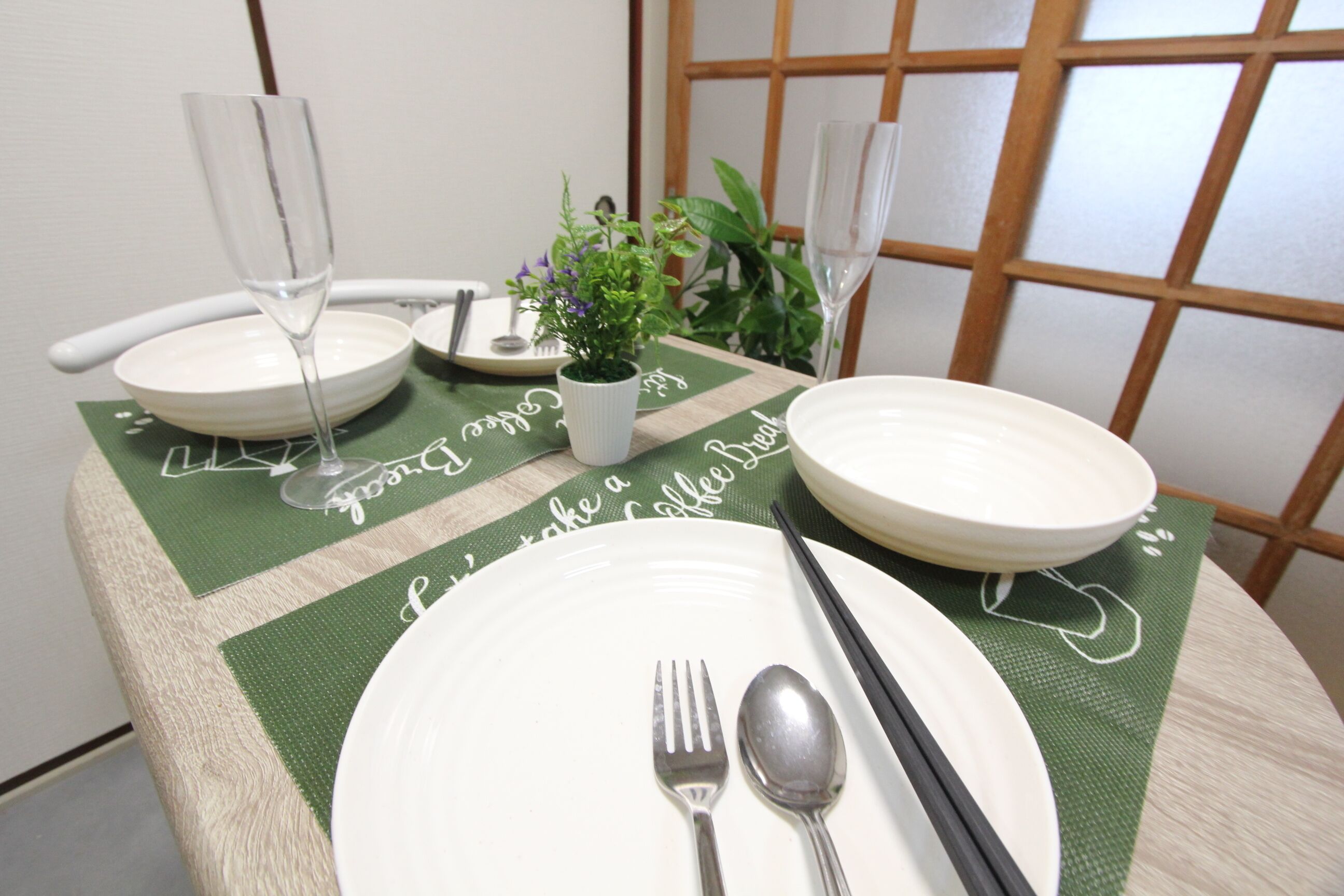 A dining table set with white plates, cutlery, and two wine glasses.