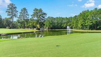 Un parcours de golf avec un green d’entraînement, un étang et des arbres en arrière-plan.