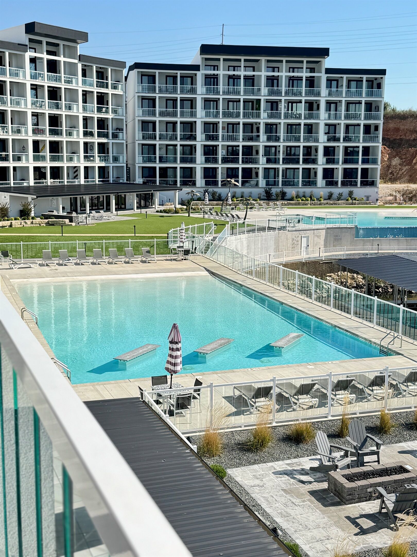 Ein Hotel mit einem großen Außenpool, mehreren Balkonen und einer angelegten Grünfläche mit Liegestühlen.