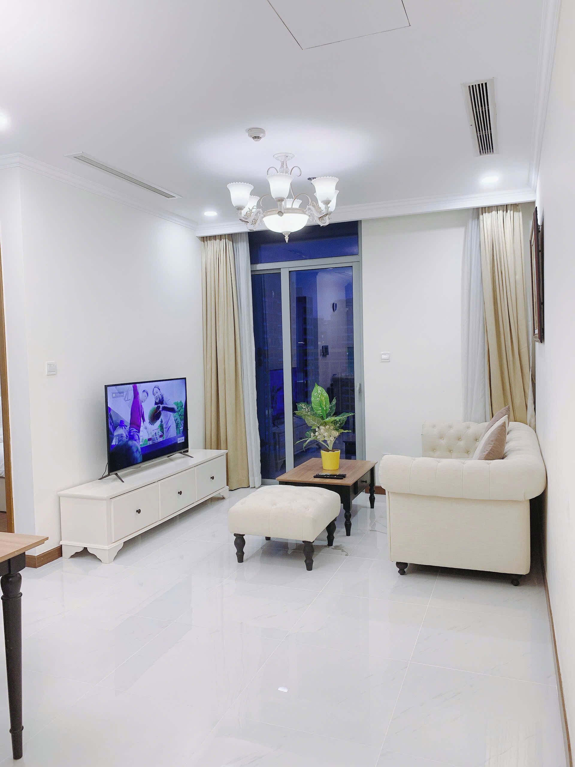 Una sala de estar moderna con un televisor de pantalla plana, un sofá blanco, una mesa de centro de madera y un reposapiés blanco.