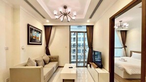 A modern living room with a sofa, a coffee table, a TV, and a large window with curtains. - Vinhomes Central Park (Ho Chi Minh City)