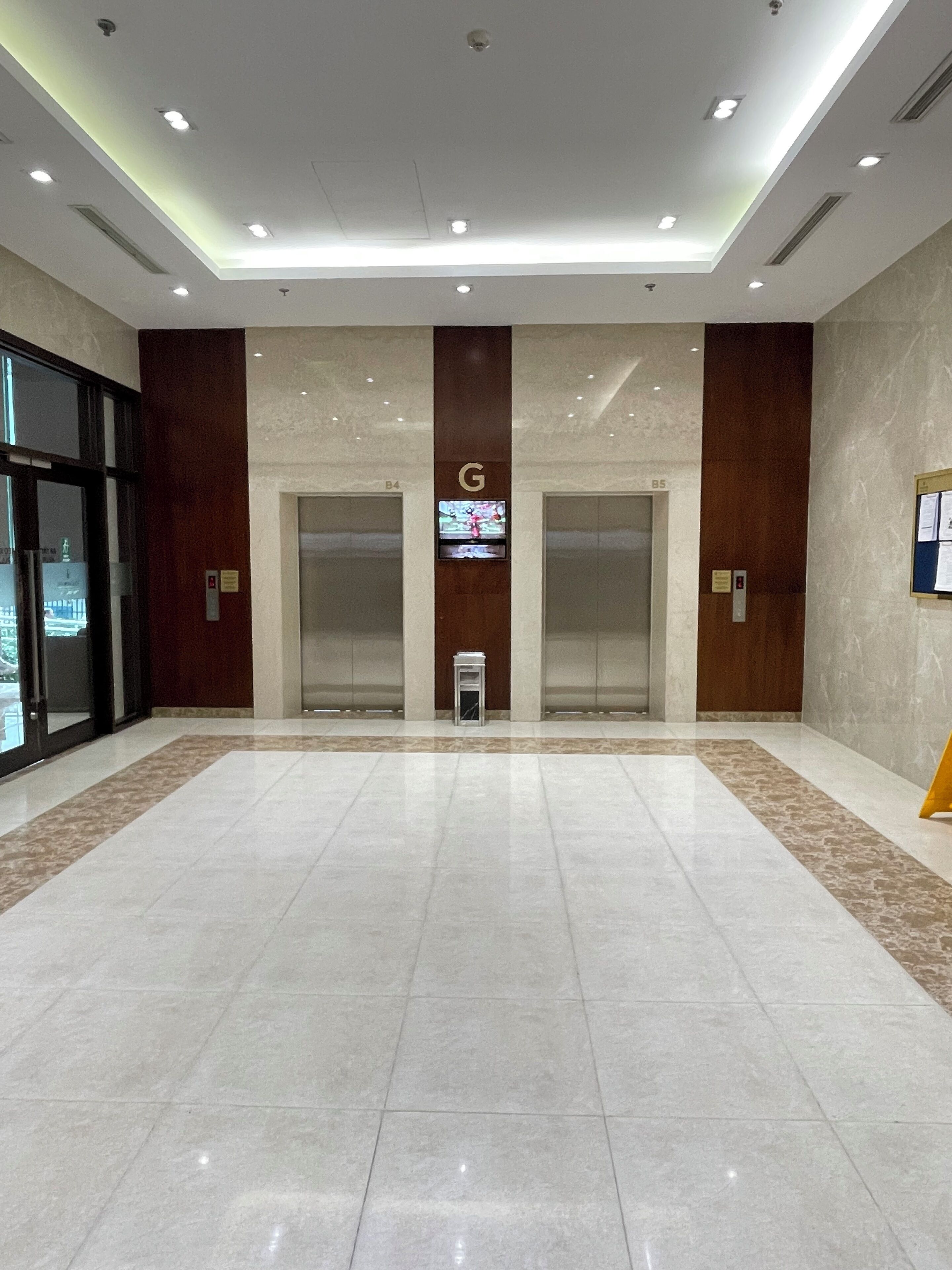 Eine großzügige Lobby mit Marmorboden, zwei Aufzügen und einer digitalen Anzeige an der Wand.
