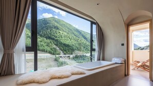 A room with a large window offering a view of a forested mountain.
